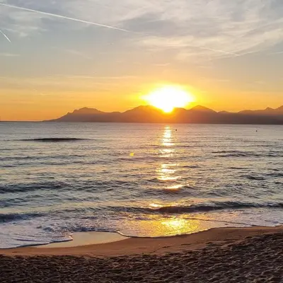 a sunset on the beach with mountains in the background at CROISETTE AZUR ONE BEDROOM APARTMENT WITH TERRACE in Cannes